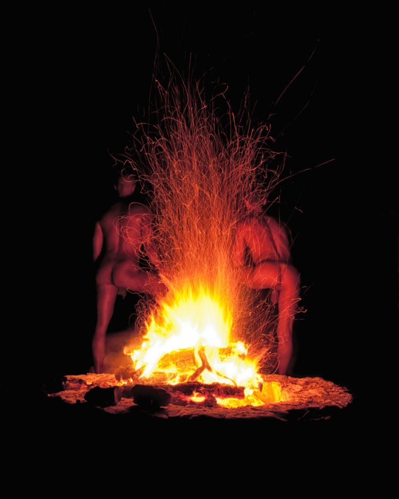 Two men standing by a campfire at night — sparks flying, firelight illuminating their backs | Trey Fox Photography Austin
