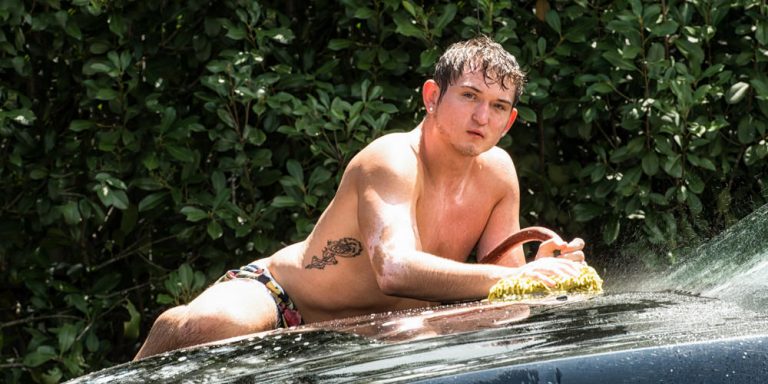 Male boudoir car wash session Houston — client on car fender with sponge by Trey Fox